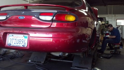 1996 Ford Taurus - A mechanic works on the rear brakes of a red 1996 Ford Taurus in a repair shop.
