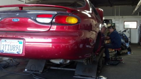 1996 Ford Taurus - A red 1996 Ford Taurus is being serviced in a garage, with a mechanic attending to the rear wheel.
