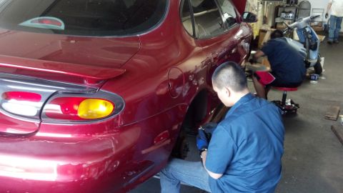 1996 Ford Taurus - Mechanic works on the rear wheel of a red 1996 Ford Taurus in a garage.