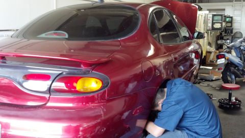 1996 Ford Taurus - Mechanic performs work on the rear wheel area of a red 1996 Ford Taurus sedan.