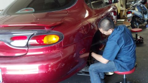 1996 Ford Taurus - A mechanic works on the rear wheel of a red Mazda RX-7 in a garage, with a scooter visible in the background.