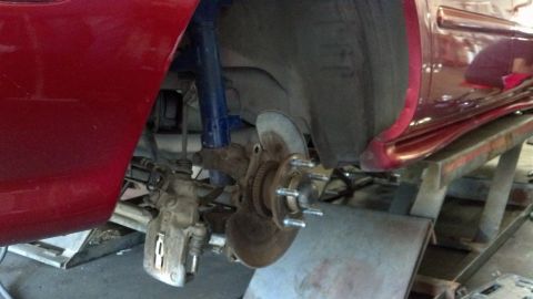 1996 Ford Taurus - Close-up of a red 1996 Ford Taurus's front brake system, showing the rotor, caliper, and suspension components.