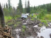 1979 Ford Bronco - A white SUV is stuck in a muddy, rocky area surrounded by trees.
