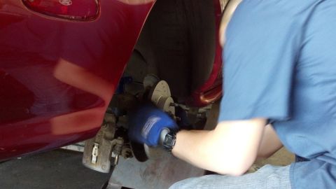 1996 Ford Taurus - A person in blue gloves is working on the brake assembly of a red vehicle.