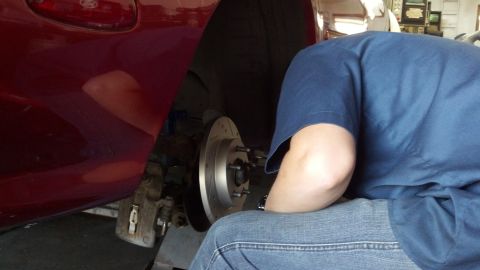 1996 Ford Taurus - A person works on the rear brake rotor and caliper of a red 1996 Ford Taurus.