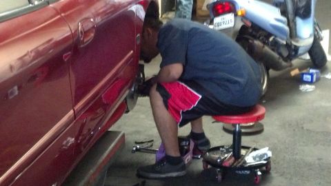 1996 Ford Taurus - A mechanic works on the brake rotors and pads of a red car, with a motorcycle visible in the background.