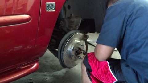 1996 Ford Taurus - A person is shown installing new drilled and slotted rotors on a red vehicle's braking system.