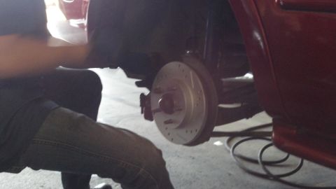 1996 Ford Taurus - A mechanic works on the rear brake assembly of a red car, installing new drilled and slotted rotors.