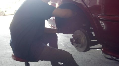 1996 Ford Taurus - A mechanic works on the rear brake rotor of a red vehicle, likely replacing brake pads and rotors.