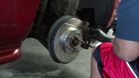 1996 Ford Taurus - A person in black gloves works on replacing the brake rotor on a red vehicle.