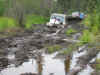 1979 Ford Bronco - Two SUVs are driving through a muddy area, likely off-roading.