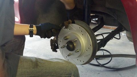 1996 Ford Taurus - A person is shown installing a new drilled and slotted brake rotor onto a vehicle's wheel hub.