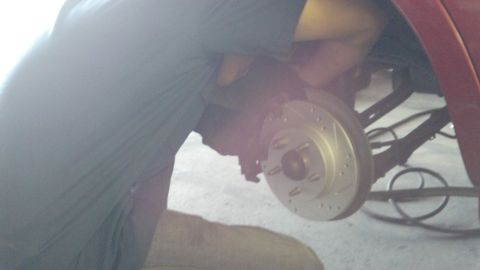 1996 Ford Taurus - A person works on the rear brake rotor and suspension of a red vehicle.