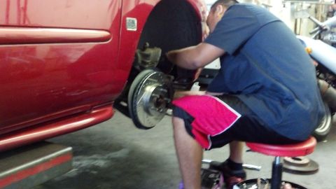 1996 Ford Taurus - Mechanic replaces brake rotor and pads on a red vehicle in a garage setting.