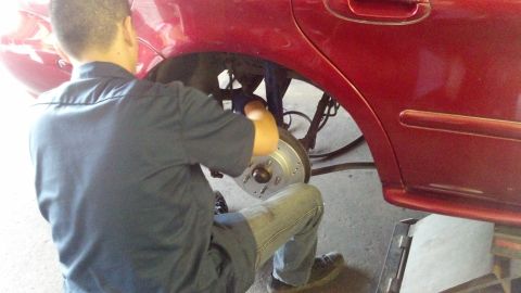 1996 Ford Taurus - A mechanic is shown installing a new drilled and slotted brake rotor on the rear wheel of a red vehicle.