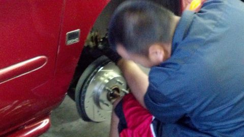 1996 Ford Taurus - Mechanic installing new drilled and slotted brake rotor on a red vehicle.