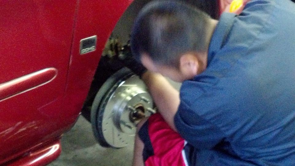 Person installing drilled brake rotor on red car wheel hub