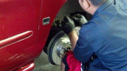 1996 Ford Taurus - A person in black gloves is replacing the brake rotor on a red vehicle.
