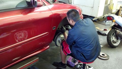 1996 Ford Taurus - Mechanic replaces brake rotors and pads on a red 1996 Ford Taurus in a garage, with a scooter visible in the background.
