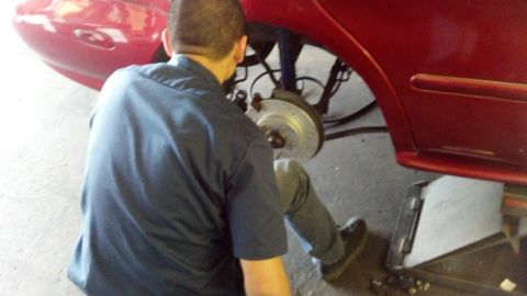 1996 Ford Taurus - Mechanic installs new drilled and slotted rotors on a red 1996 Ford Taurus, as seen from the rear quarter panel.