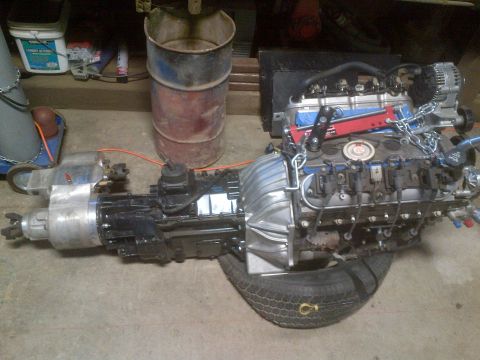 1985 Jeep CJ7 - Engine and transmission assembly, likely for a project vehicle, rests on a tire in a workshop.
