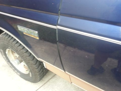 1994 Ford Bronco - Close-up of the side panel and fender of a dark blue SUV, showing trim details and a tire.