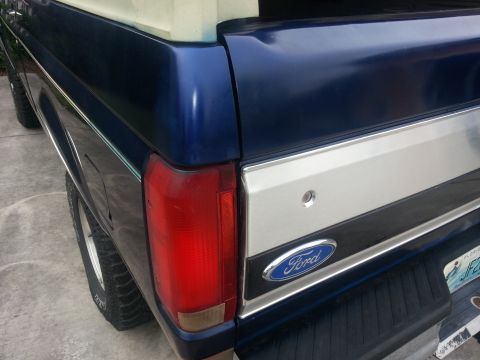 1994 Ford Bronco - The rear of a blue Ford pickup truck shows its taillight and a chrome trim piece with the Ford logo.