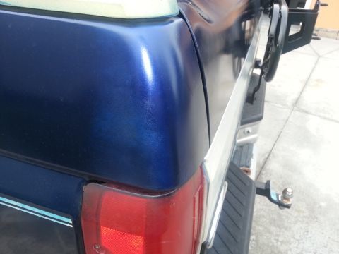 1994 Ford Bronco - Close-up of the rear corner of a blue metallic SUV, showing the taillight and chrome trim.