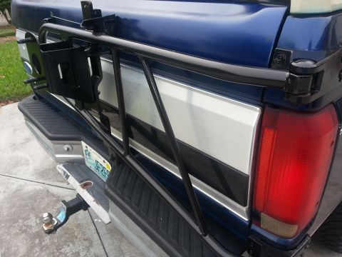 1994 Ford Bronco - The rear of a blue pickup truck shows a spare tire carrier mounted on the tailgate and a trailer hitch below the bumper.