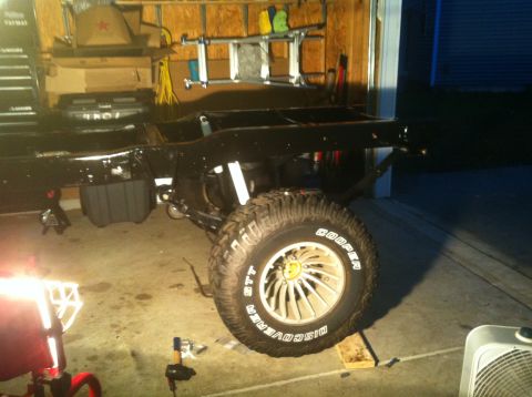 1979 Ford Bronco - The chassis and suspension of a vehicle are visible in a garage setting, with a large tire mounted.