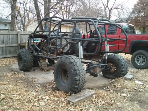 1986 Ford Bronco - A custom-built off-road buggy is shown with a roll cage and large tires, with a red pickup truck parked behind it.