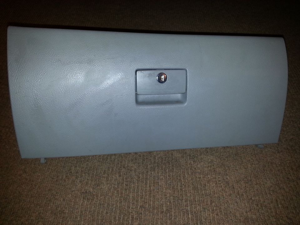 Gray plastic glove box door with a lock, resting on carpet