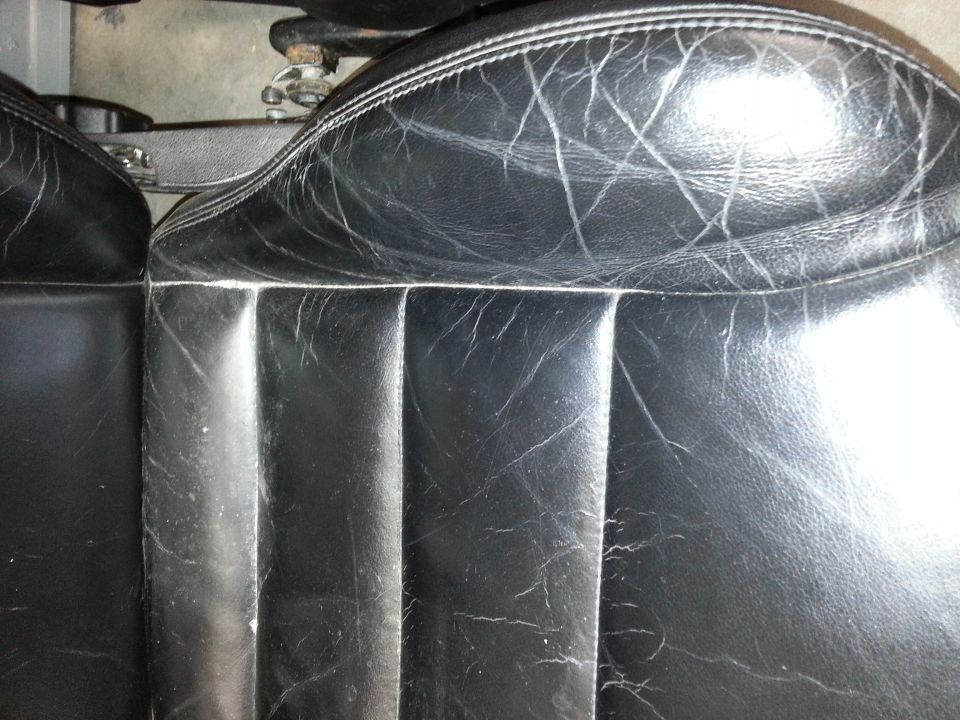 Close-up of cracked black leather car seats with white stitching
