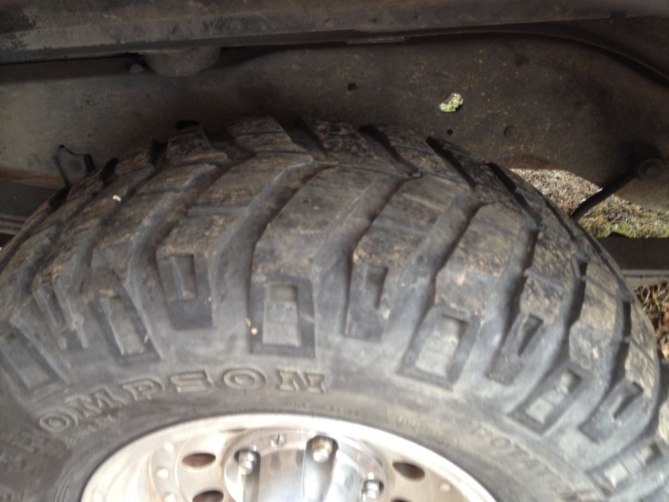 Close-up of a large off-road tire with 'OMPSON' visible on the sidewall, attached to a vehicle's suspension