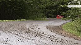 2000 Mercury Grand Marquis - A rally car navigates a dusty dirt road, with trees lining the path and a red sign visible in the distance.