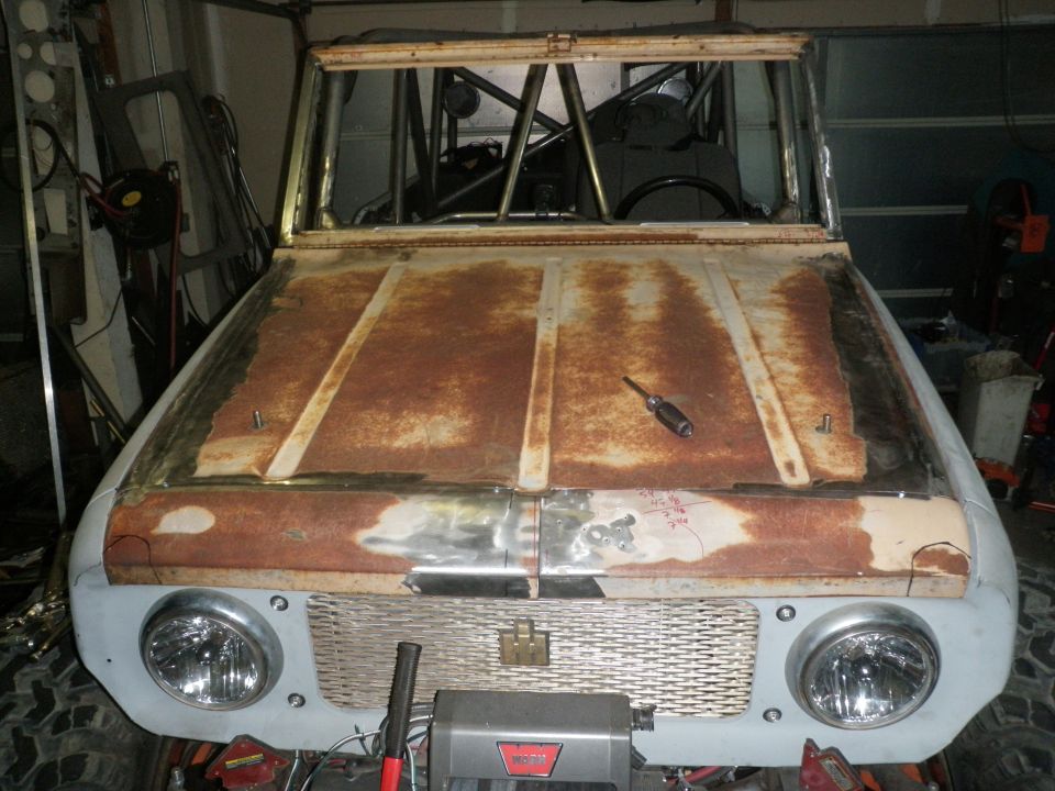 Front view of a rusty 1961 International Scout 800 with a roll cage inside