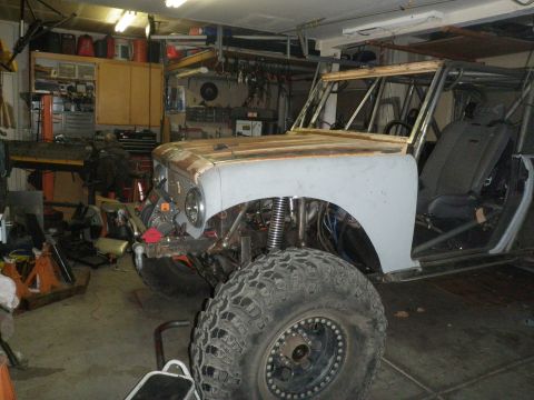 1961 International Scout 800 - A partially completed off-road vehicle sits in a cluttered garage, showing its custom roll cage and large tires.
