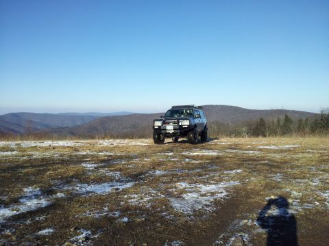 2003 Nissan Frontier - A modified SUV sits on a hilltop overlooking a valley under a clear blue sky.
