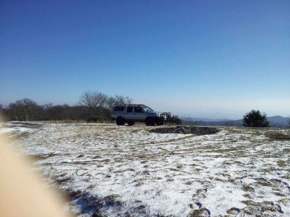 Silver 2003 Nissan Frontier pickup truck with canopy and roof rack parked on a snowy hill