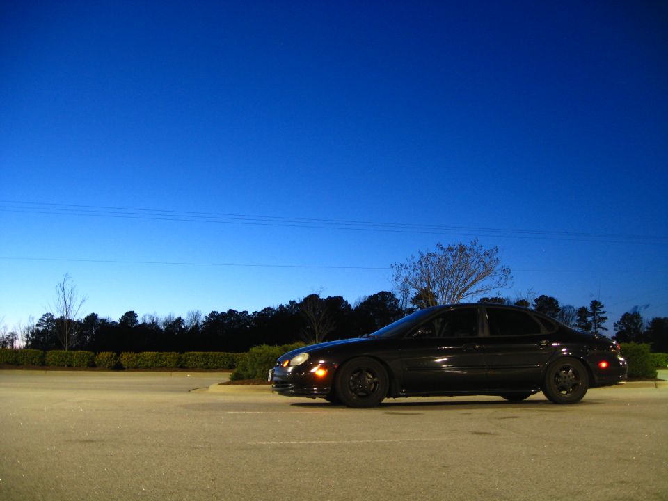 Black 1997 Ford Taurus parked on asphalt with a clear blue sky overhead