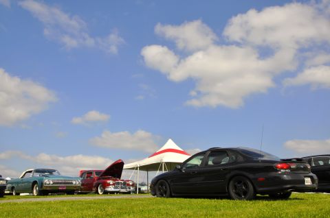 1997 Ford Taurus - Several cars are parked on a grassy field under a partly cloudy sky.