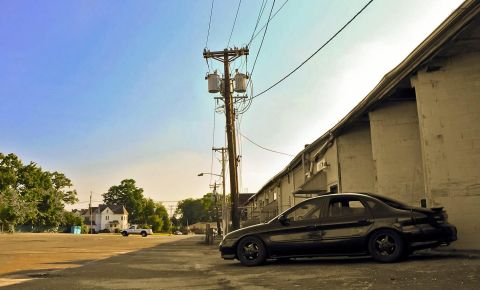 1997 Ford Taurus - A black 1997 Ford Taurus is parked alongside a weathered building under a bright blue sky.