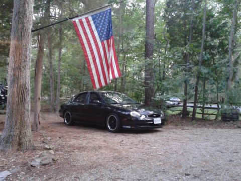 1997 Ford Taurus - Black 1997 Ford Taurus sedan parked in a wooded area under an American flag.