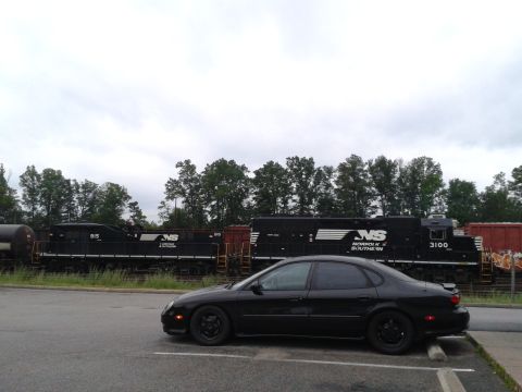 1997 Ford Taurus - A black sedan is parked beside a Norfolk Southern train on a cloudy day.