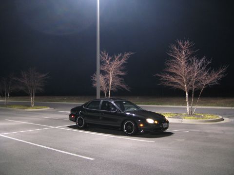 1997 Ford Taurus - A black 1997 Ford Taurus is parked in a dimly lit parking lot under a streetlamp.