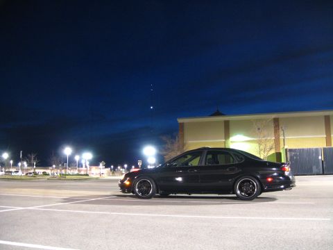 1997 Ford Taurus - Side view of a black 1997 Ford Taurus parked in a lot at night.