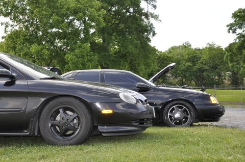 1997 Ford Taurus - Two black sedans are parked side-by-side on a grassy area with trees in the background.