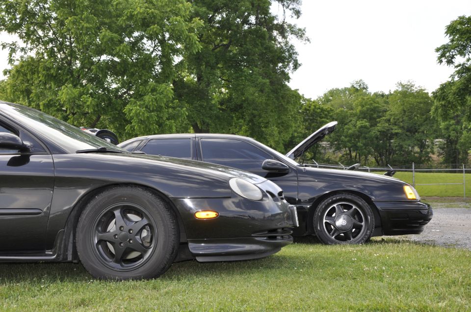 Two black sedans parked on grass, one with hood open