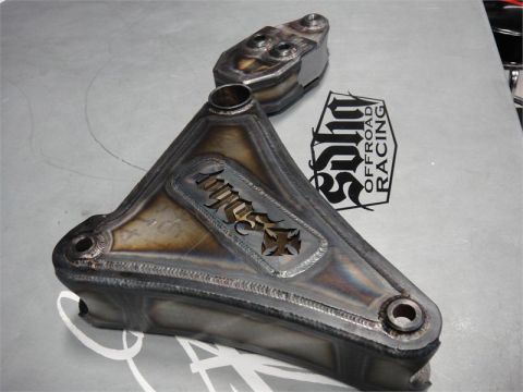1988 Ford Bronco - Custom metal part with 'Toyo' logo and cross cutout, alongside another metal component, on a grey surface.