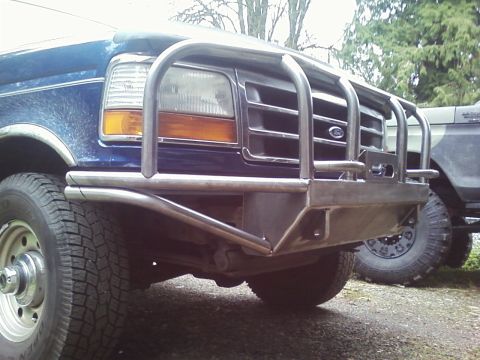 1989 Ford Bronco - A blue Ford F-Series truck is equipped with a heavy-duty brush guard and winch mount on its front end.